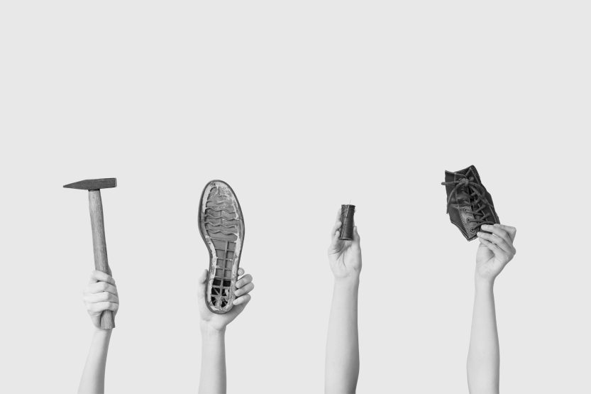 Female hands with shoe pieces, hammer and sewing thread on white